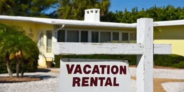 A Vacation Rental Sign in front of a yellow one story home on the beach.