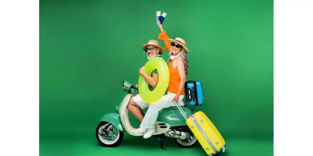 Cheerful middle aged asian woman in sun hat holding passports near husband holding swim ring while riding moped on green