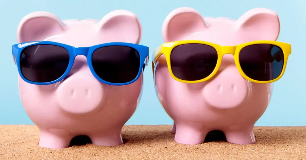 Two pink piggy banks on a beach with sunglasses.