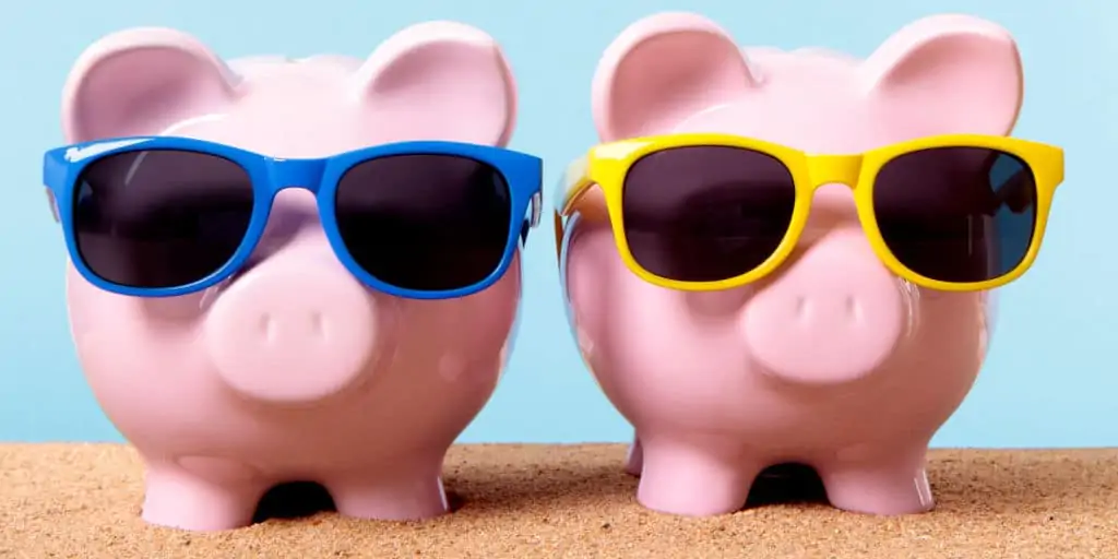 Two pink piggy banks on a beach with sunglasses.