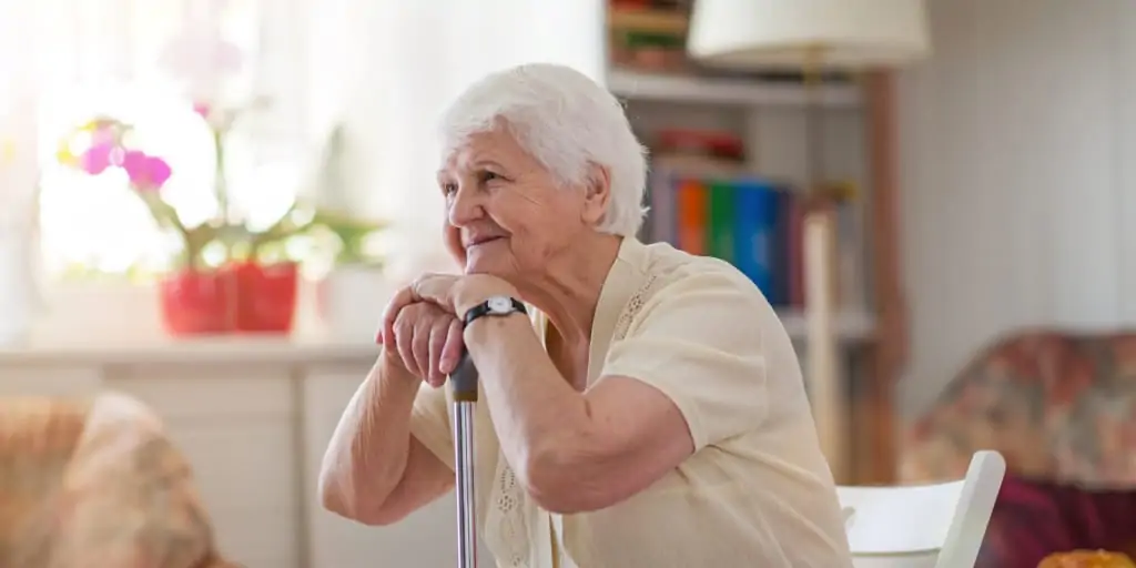 smiling white haired senior woman sitting and resting her hands and head on the top of her cane