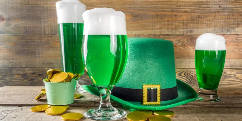 Traditional irish alcohol for St Patrick's day party. Different glasses with green beer, with golden chocolate coins decor and green leprechaun hat. Old rustic wooden background