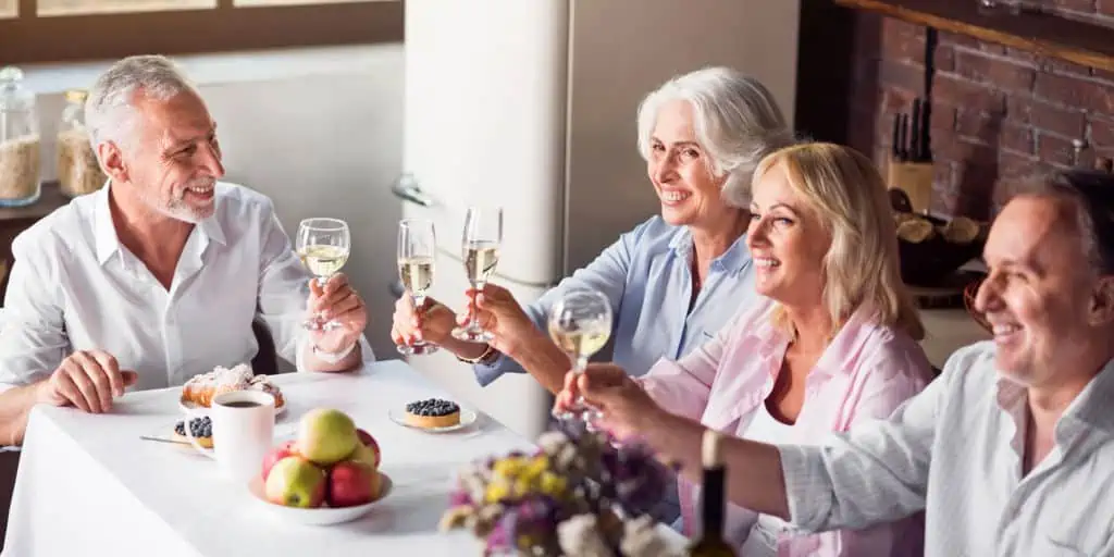 House guests and hosts sitting at kitchen table drinking champagne and enjoying dessert